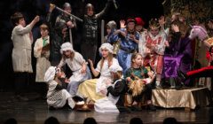 Children dressed in various costumes perform on stage in a theatrical production.