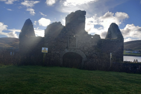 Ruins of an old stone structure on a sunny day with a cautionary sign in the foreground.