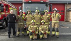 Group of firefighters standing in front of a fire truck at the station.