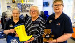 Three volunteers at a lifeboat charity shop posing with merchandise.