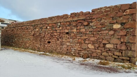 A weathered stone wall on a snow-dusted ground with patches of grass.