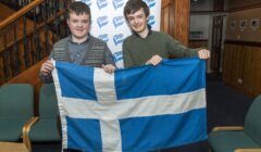 Two individuals holding the flag of scotland indoors.