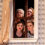 Four women of varying ages peer through a window frame on stage, suggesting a scene from a theatrical performance.