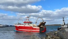 Fishing trawler returning to port under a cloudy sky.