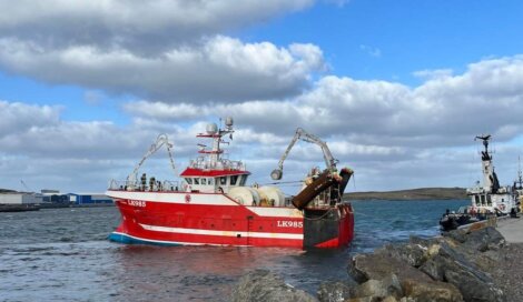 Fishing trawler returning to port under a cloudy sky.