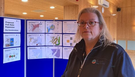 Woman in uniform standing in front of informational posters about a proposed fish holm expansion.