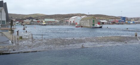 Harbor with boats and buildings on an overcast day with visible water level rising over the dock.