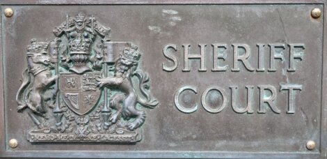 Bronze plaque with the text "sheriff court" beneath a relief of a coat of arms flanked by two heraldic beasts.