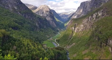 Lush green valley with a winding river flanked by steep, shadowed mountain cliffs under a cloudy sky.