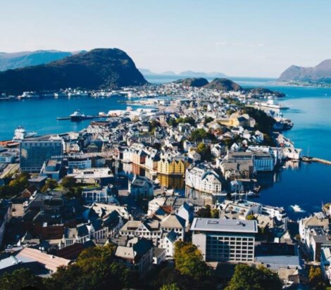 Aerial view of a coastal city with clustered buildings surrounded by water and mountains under a clear sky.