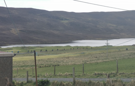 A scenic view of a rural landscape featuring a lake surrounded by rolling hills, with a line of power poles and cables in the foreground.