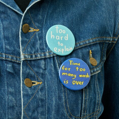 Denim jacket with two pins: one saying "too hard to explain" and the other "time for too many words is over.