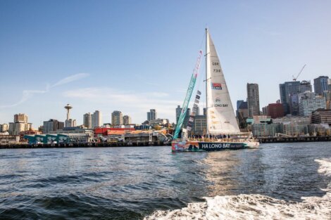 A sailboat featuring "ha long bay, viet nam" on its side sails in a harbor with city skyline and space needle in the background.