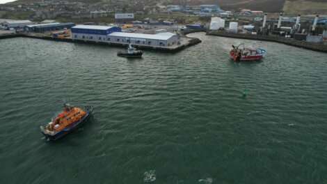 Aerial view of boats near a harbor with industrial buildings along the coastline.