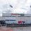 Front view of aberdeen international airport building with two scottish flags flying and a shuttle bus outside.