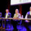 Four panelists sitting at a table on stage at a conference, with a banner reading "shetland hjaltland" in the background.