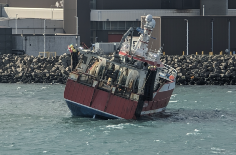 Sinking ship partially submerged and tilting dangerously near a rocky shoreline.