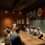 A bartender presenting to seated patrons at a dimly lit tasting room decorated with wall art and serving beer samples.