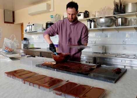 A man pouring melted chocolate into molds on a kitchen counter surrounded by cooking utensils and containers.