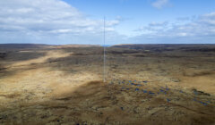 Aerial view of a barren landscape with sparse vegetation and scattered blue ponds under a cloudy sky.