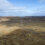 Aerial view of a barren landscape with sparse vegetation and scattered blue ponds under a cloudy sky.