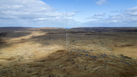 Aerial view of a barren landscape with sparse vegetation and scattered blue ponds under a cloudy sky.