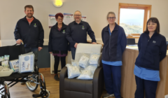 Five adults standing in a room with medical supplies and equipment, smiling at the camera.