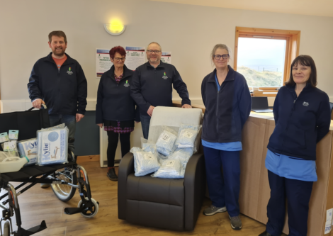 Five adults standing in a room with medical supplies and equipment, smiling at the camera.