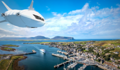 A large white airship with "AirLines" written on it flies over a coastal town with a marina and green hills in the background.