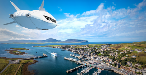 A large white airship with "AirLines" written on it flies over a coastal town with a marina and green hills in the background.