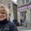 Woman smiling in front of a tourist center with stone buildings and a man in the background.