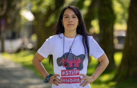 Person standing outdoors wearing a "Stop Rosebank" t-shirt, with hands on hips and trees in the background.