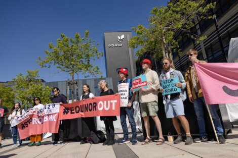 People are standing in front of an Equinor building, holding signs and banners with messages including "STOP BAY DU NORD" and "#EQUINOROUT" in a protest.