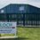 A green and white "Tulloch Developments" sign in front of a blue industrial building with a green fence under a clear sky.