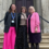 Three women stand on stairs in front of a building. The woman on the left wears a black blazer and pink pants, the woman in the middle wears a black and white polka dot skirt, and the woman on the right wears a pink blazer.