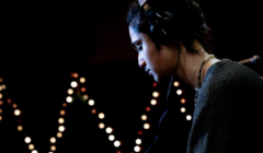 Person wearing headphones, looking down, with a backdrop of blurred lights.