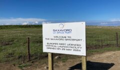 Sign at the SaxaVord UK Space Port reading: "Welcome to the SaxaVord Spaceport - Europe's first licensed vertical launch facility opened on 29 May 2024," against a backdrop of grass and clear sky.