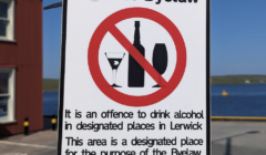 Sign on a pole stating "Shetland Islands Council Alcohol Byelaw." It is an offense to drink alcohol in designated places in Lerwick. Maximum penalty £500. The sign shows a no alcohol symbol.