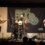 Three musicians performing at the shetland folk festival, featuring a guitarist, a drummer, and an accordion player on stage.