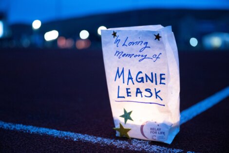 A luminary bag labeled "In loving memory of Magnie Leask" with stars and a candle inside, placed on a track during a Relay For Life event.