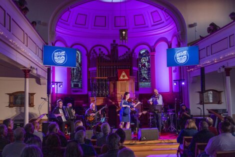 A live band performs in a church converted into a concert venue, featuring a diverse array of instruments and an attentive audience.