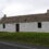 A traditional whitewashed stone cottage with a thatched roof, two chimneys, and a single door, set against a cloudy sky.