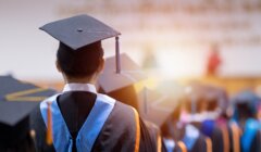 Students in graduation caps and gowns face forward in an indoor ceremony.