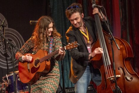 A female guitarist and a male double bassist performing together on stage, both smiling and focused on their instruments.