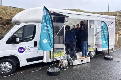 Mobile driving simulation trailer parked with several people standing inside learning about driving tests, affiliated with south lanarkshire college and local councils.