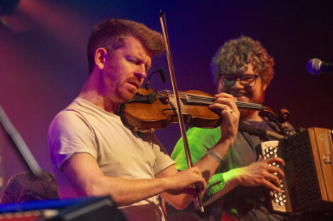 Two musicians on stage; one playing a violin and the other an accordion, both focused intensely on their performance.