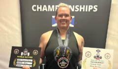 A person smiling, holding two world record certificates and wearing a medal at the scottish championships event.