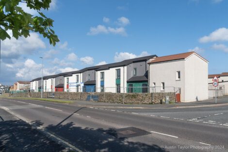 Row of modern, multi-colored townhouses behind a stone wall on a sunny day, with a street and some traffic signs in the foreground. Photo credit to Austin Taylor Photography 2024.