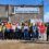 A group of workers wearing high-visibility jackets and holding Unite union posters stand outside a building labeled "Sullom Voe Terminal," with barbed wire visible above the entrance.