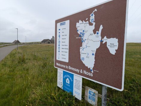 A signboard at the entrance of Bressay & Noss displays a map of the area with information on various landmarks and services.